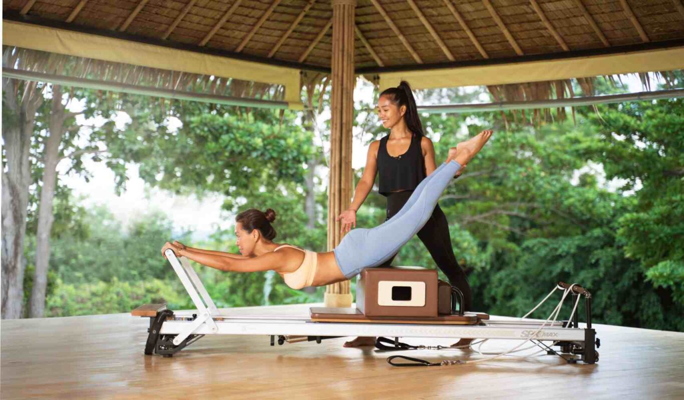 A trainer guiding a guest through a Reformer Pilates exercise in an open-air pavilion at Absolute Sanctuary